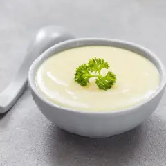 Kremowa zupa, idealna na dietę bezresztkową, ozdobiona listkiem pietruszki. Obok leży łyżka.