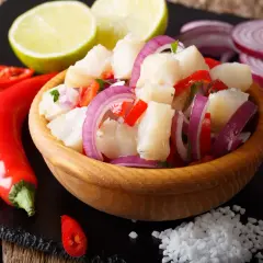 Pyszne ceviche z kawałkami ryby, czerwoną cebulą, papryką i chili, podane z limonką i solą.