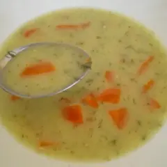 Łyżka zupy śmietanowej z marchewką i koperkiem na białym talerzu.