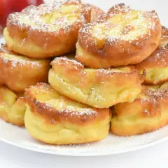 Złociste racuchy z jabłkami, posypane cukrem pudrem. Przepis babci na pyszne, domowe ciasto.