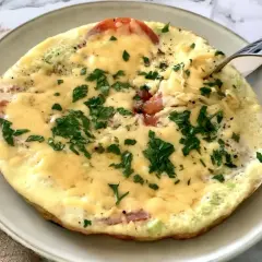 Pyszne śniadanie keto: omlet z pomidorami, serem i natką pietruszki, właśnie nabierany widelcem. Idealny początek dnia.
