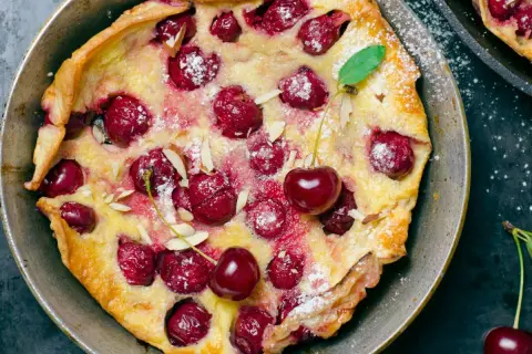 Puszysty omlet z białek z wiśniami i płatkami migdałów, posypany cukrem pudrem. Idealny deser na każdą okazję.