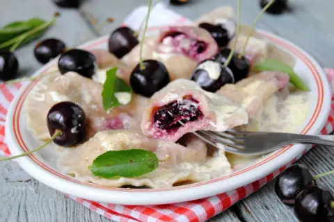 Pyszne pierogi z czereśniami, polane śmietaną, ozdobione świeżymi owocami i listkami mięty. Idealne na letni deser.