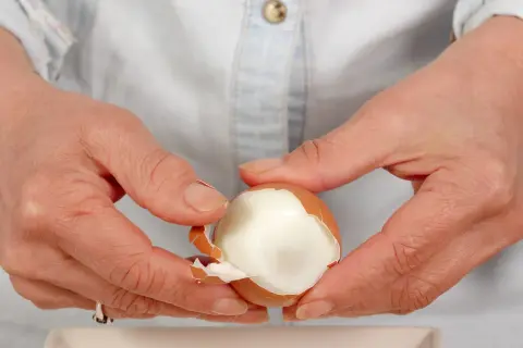 Dłonie obierają jajko na twardo. Czy jajka podnoszą cholesterol? To pytanie nurtuje wiele osób, ale współczesne badania pokazują, że umiarkowane spożycie jajek jest bezpieczne.