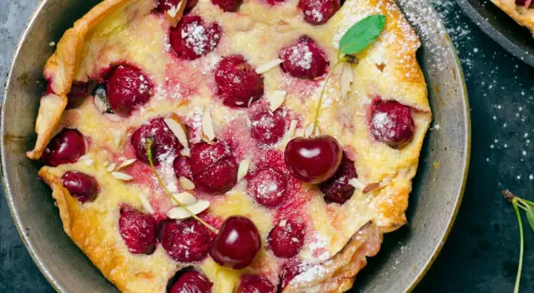 Puszysty omlet z białek z wiśniami i płatkami migdałów, posypany cukrem pudrem. Idealny deser na każdą okazję.