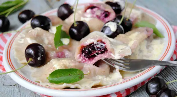 Pyszne pierogi z czereśniami, polane śmietaną, ozdobione świeżymi owocami i listkami mięty. Idealne na letni deser.