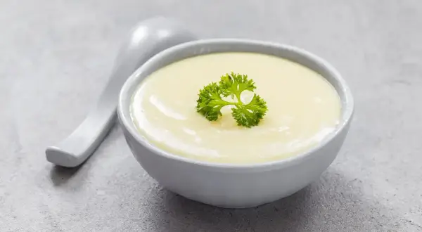 Kremowa zupa, idealna na dietę bezresztkową, ozdobiona listkiem pietruszki. Obok leży łyżka.