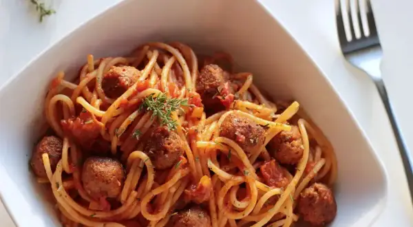 Pyszne spaghetti z klopsikami w sosie pomidorowym, udekorowane gałązką tymianku. Idealne pytanie: jakie przyprawy do spaghetti?