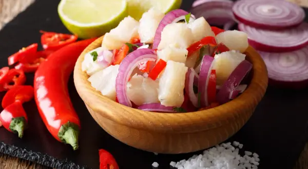 Pyszne ceviche z kawałkami ryby, czerwoną cebulą, papryką i chili, podane z limonką i solą.