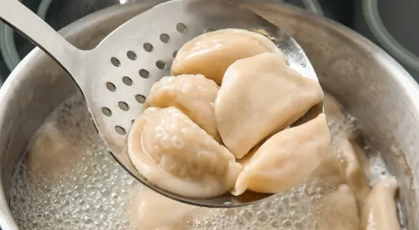 Gorące pierogi z serem, gotowane według przepisu babci, wyjmowane łyżką cedzakową z bulgoczącego garnka.