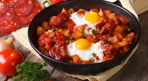 Pyszny obiad z jajek z ziemniakami, chorizo i groszkiem w patelni.
