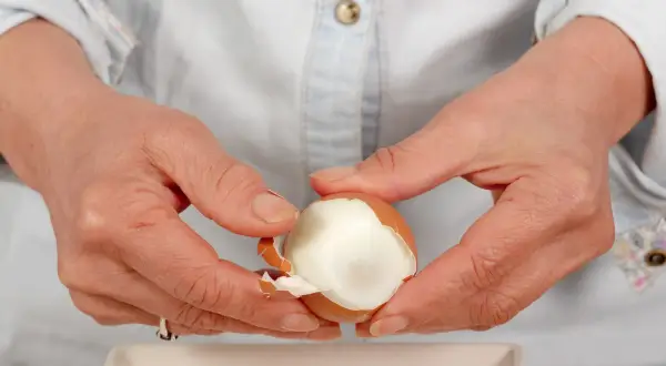 Dłonie obierają jajko na twardo. Czy jajka podnoszą cholesterol? To pytanie nurtuje wiele osób, ale współczesne badania pokazują, że umiarkowane spożycie jajek jest bezpieczne.