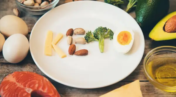 Litery KETO ułożone z sera, orzechów, brokuła i jajka. Czy dieta keto jest zdrowa? Obok łosoś, awokado, oliwa.