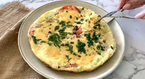 Pyszne śniadanie keto: omlet z pomidorami, serem i natką pietruszki, właśnie nabierany widelcem. Idealny początek dnia.