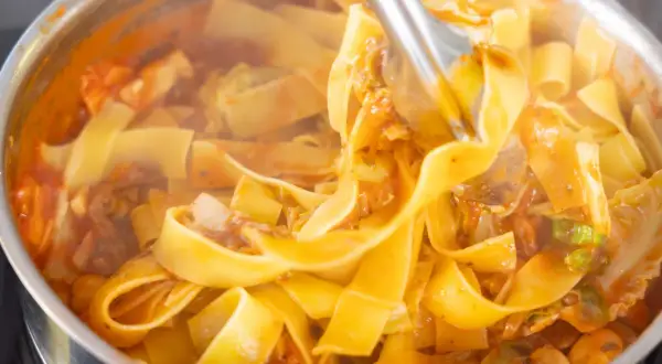 Szybki obiad z makaronem w sosie pomidorowym z warzywami. Gorące, parujące tagliatelle w garnku, gotowe do podania.