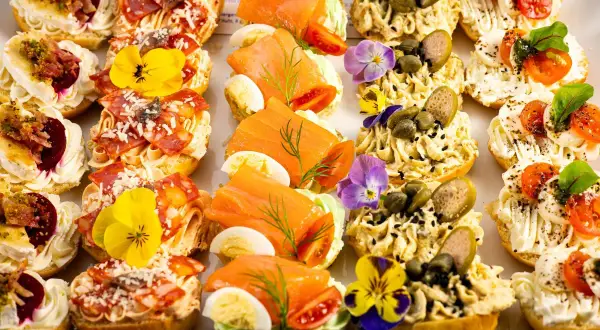 Kolorowe przekąski na talerzu: łosoś, salami, pasztet, warzywa i jadalne kwiaty. Idealne na szybkie śniadanie.