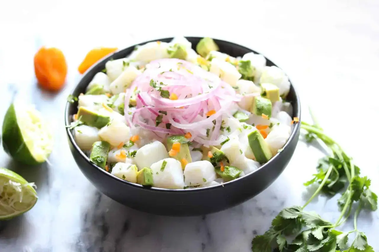 Pyszne ceviche z kawałkami ryby, awokado, czerwoną cebulą i kolendrą, podane w czarnej misce z limonką.