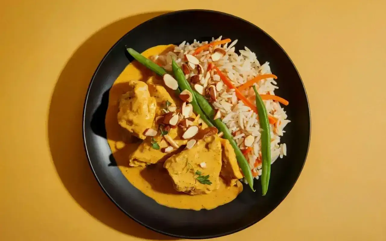 Aksamitny kurczak curry w kremowym sosie, podany z ryżem basmati, fasolką szparagową i płatkami migdałów.