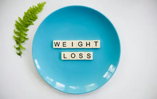 Niebieski talerz z literami "WEIGHT LOSS" i gałązką paproci. Idealny do planowania diety 10 kg w 2 tygodnie jadłospis.