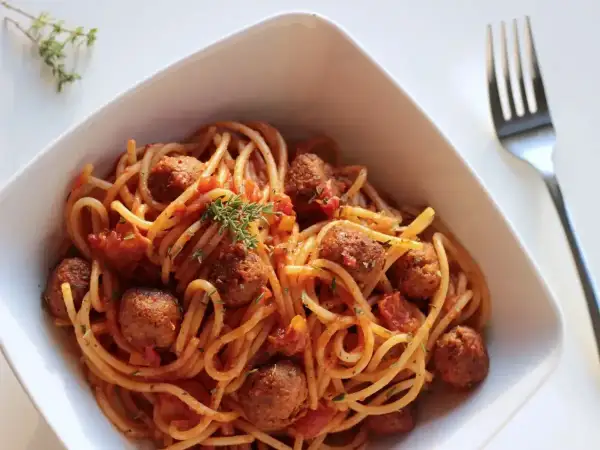 Pyszne spaghetti z klopsikami w sosie pomidorowym, udekorowane gałązką tymianku. Idealne pytanie: jakie przyprawy do spaghetti?