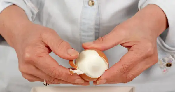 Dłonie obierają jajko na twardo. Czy jajka podnoszą cholesterol? To pytanie nurtuje wiele osób, ale współczesne badania pokazują, że umiarkowane spożycie jajek jest bezpieczne.
