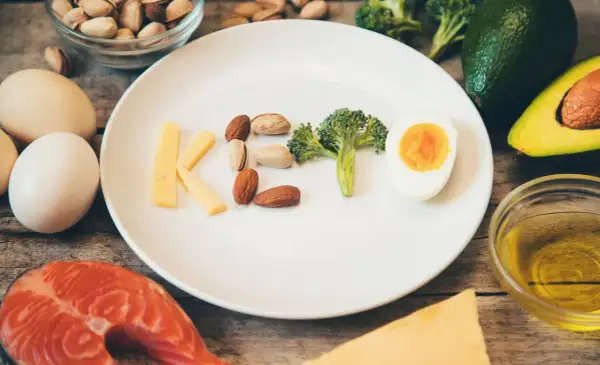 Litery KETO ułożone z sera, orzechów, brokuła i jajka. Czy dieta keto jest zdrowa? Obok łosoś, awokado, oliwa.