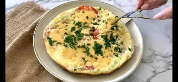 Pyszne śniadanie keto: omlet z pomidorami, serem i natką pietruszki, właśnie nabierany widelcem. Idealny początek dnia.