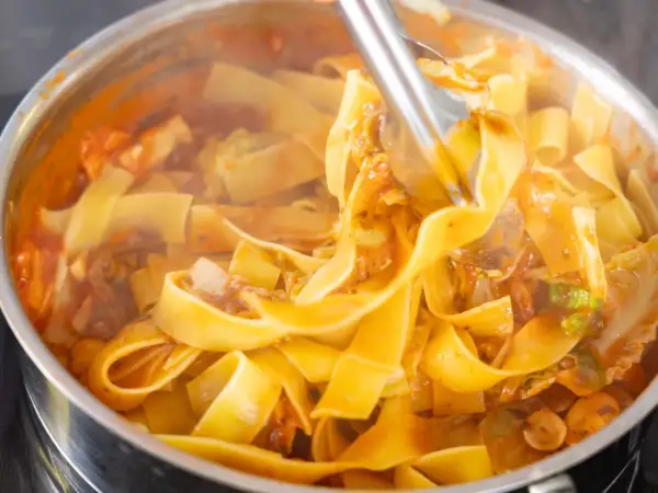 Szybki obiad z makaronem w sosie pomidorowym z warzywami. Gorące, parujące tagliatelle w garnku, gotowe do podania.